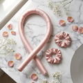 CurlBloom blush pink silk heatless curling wand headband and matching scrunchies flat-lay on white marble with rose petals